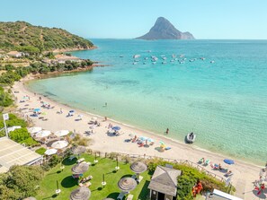 Una playa con agua turquesa cristalina, una montaña al fondo y varios barcos.