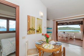 A room with a bed, a dining table with chairs, a view of the sea, and artwork on the wall.