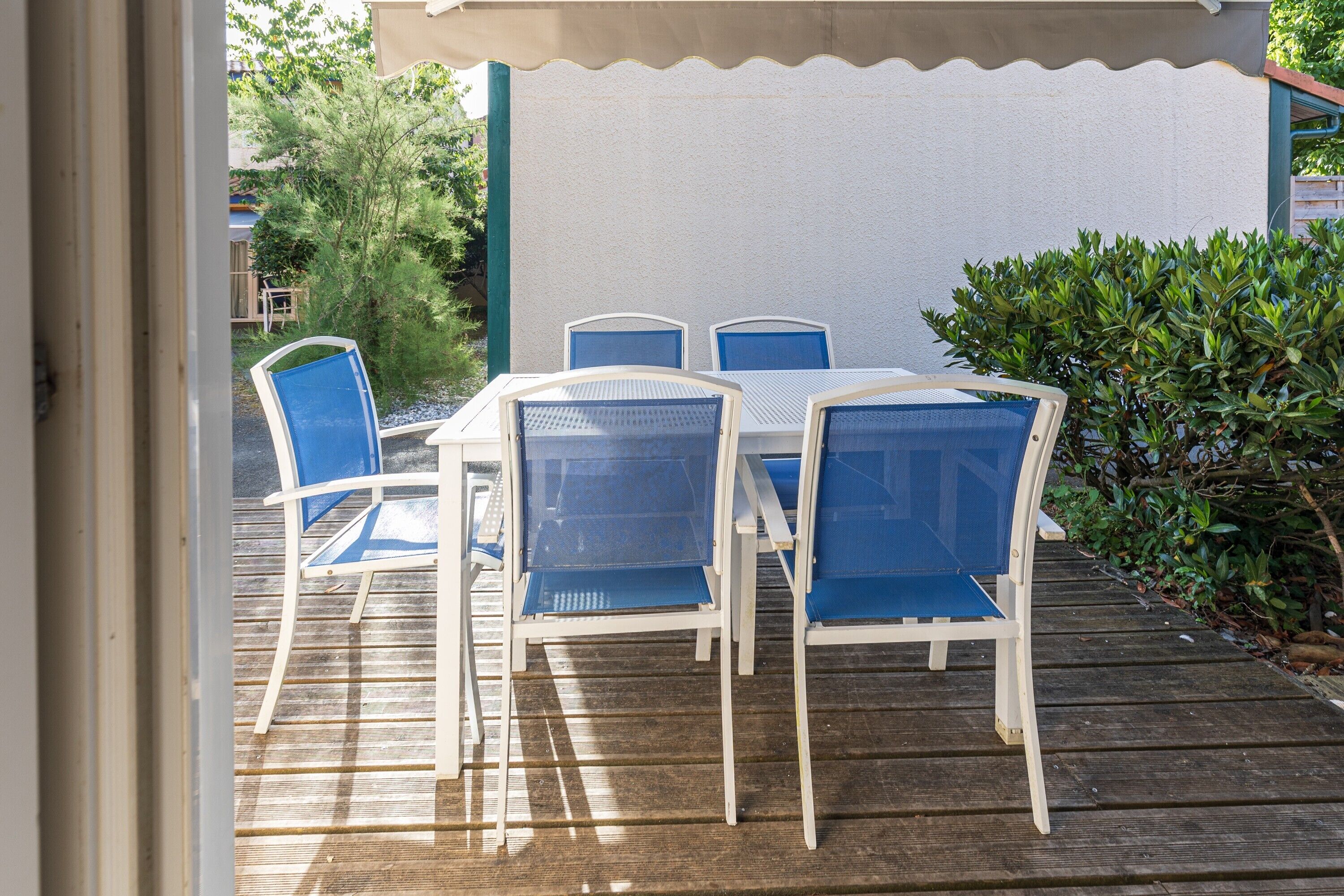 Une terrasse avec une table blanche et des chaises bleues, entourée de verdure.