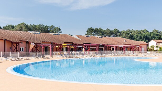 A swimming pool with lounge chairs, a covered area with a roof, and a building with a tiled roof.