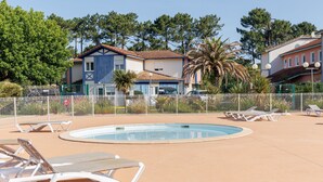 A swimming pool with lounge chairs, a fenced area, and buildings in the background.