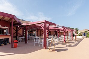 Un restaurante al aire libre con toldo rojo, mesas y sillas blancas.