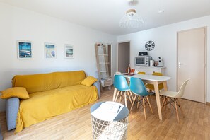 Une pièce avec un canapé jaune, une table à manger avec des chaises, une lampe blanche et un four à micro-ondes posé sur une étagère.