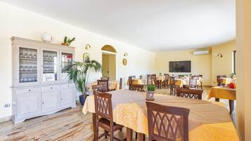 Un comedor con una mesa grande, sillas, un armario con puertas de vidrio y un televisor en la pared.