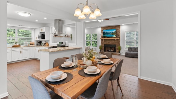 Eine moderne Küche mit weißen Schränken, einem Holzespeisetisch für vier Personen und einem Kamin im Wohnbereich.