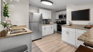 Een moderne keuken met witte kastjes, roestvrijstalen apparatuur, granieten werkbladen en een houten vloer.