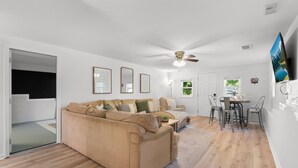 Een moderne woonkamer met een beige bank, een eethoek met tafel en stoelen, en een plafondventilator.