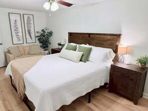 A bedroom with a large bed, a wooden nightstand, a ceiling fan, and framed wall art. - Modern 1 BR Basement Suite Near LakePoint & KSU (Acworth)