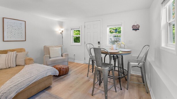 Een kamer met een bed, een bank, een eettafel met stoelen, een lamp en een ingelijst schilderij aan de muur.