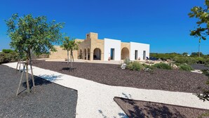 Un bâtiment moderne à la façade beige, doté d’arcades et d’un patio aménagé avec des espaces de détente en plein air.