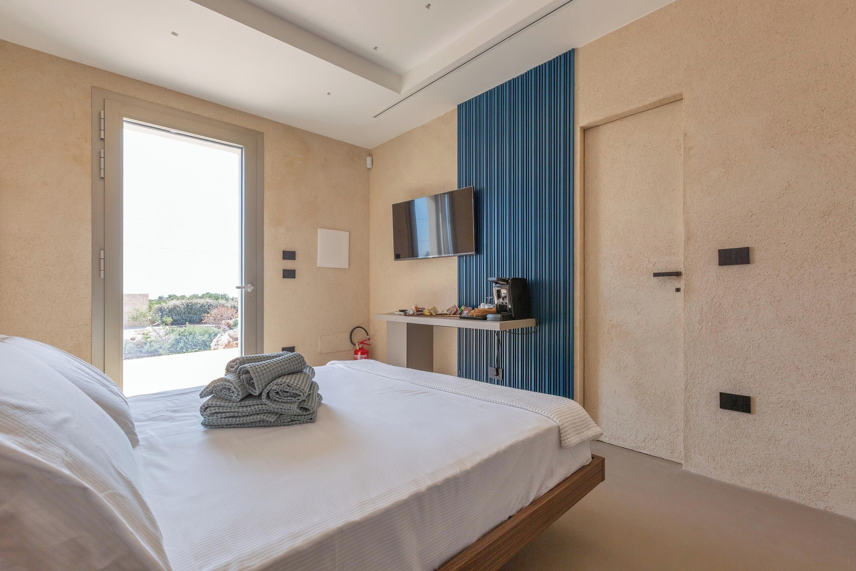 Una habitación de hotel moderna con una cama grande, un televisor fijado a la pared y vistas al exterior a través de una puerta.