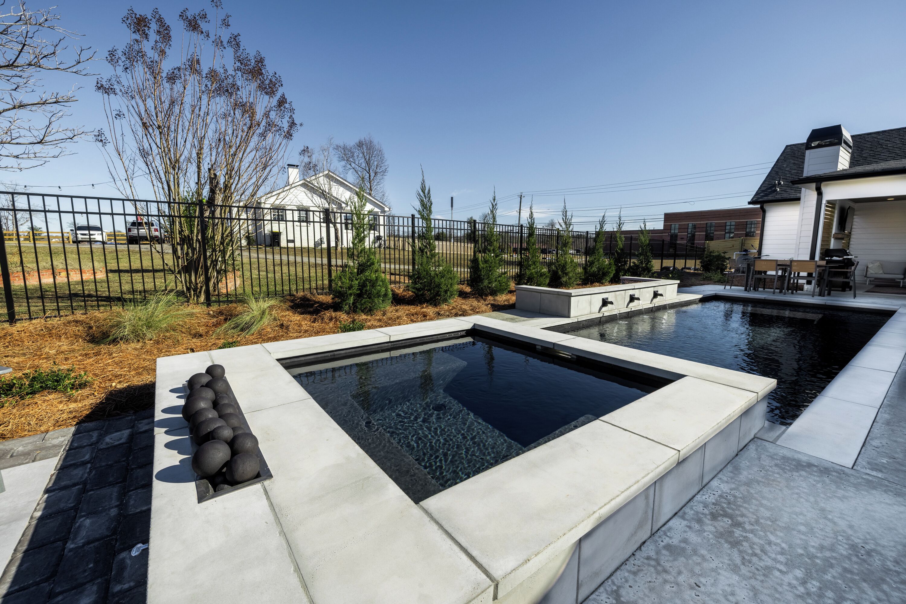 A swimming pool with a geometric design, surrounded by a fence and landscaping.