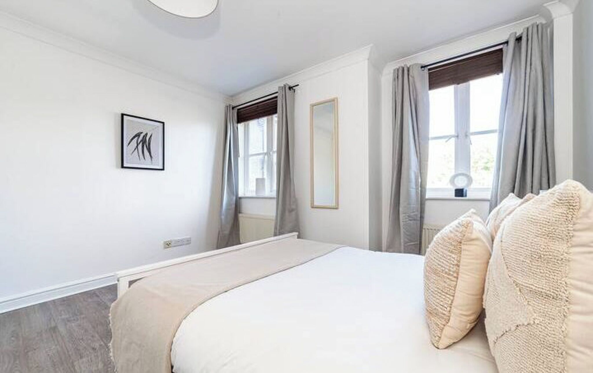A bedroom with a bed, a window with curtains, a wall-mounted mirror, and a framed picture.