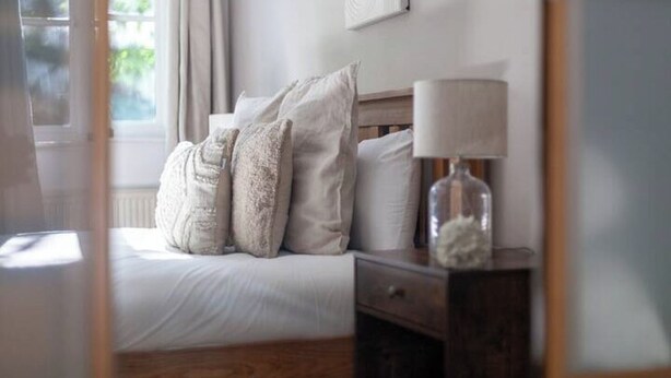 A neatly made bed with pillows and a bedside table with a lamp and a glass bottle. - Comfortable 2-Bed Apartment Near Brixton (London)