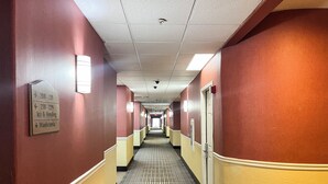 Pasillo de hotel con señalización direccional para habitaciones y servicios, piso estampado e iluminación empotrada en el techo.