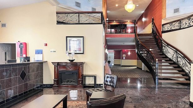 Un vestíbulo de hotel con una recepción, una chimenea, una escalera y vistas al piso superior.
