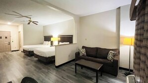 Habitación de hotel con dos camas, un sofá, una mesa de centro, un ventilador de techo y una lámpara.