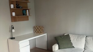 Ein modernes Schlafzimmer mit einem weißen Schreibtisch, einer weißen Couch und einem grünen Kissen.