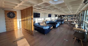 A modern lounge area with blue sofas, a dartboard, and a wooden partition. - Dove Close 21 Static Caravan Hoburne Devon Bay (Paignton)