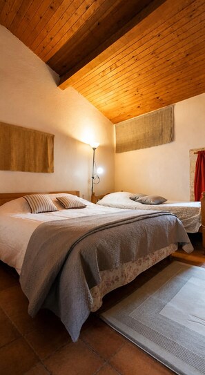 A bedroom with two beds, a wooden ceiling, a wall-mounted light, and a red curtain.