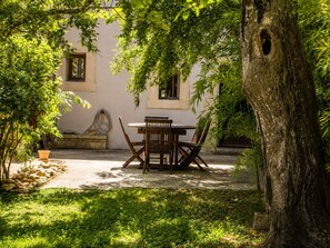 Une terrasse avec une table et des chaises, entourée de verdure et d’un arbre.