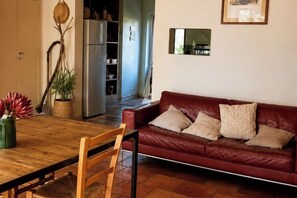 A living room with a red leather sofa, wooden dining table, and chairs. There is a kitchen area in the background.