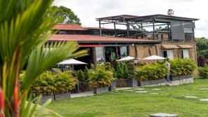 A modern building with a red roof, outdoor seating, and lush greenery. - MAHAWI RESORT (Calarca)
