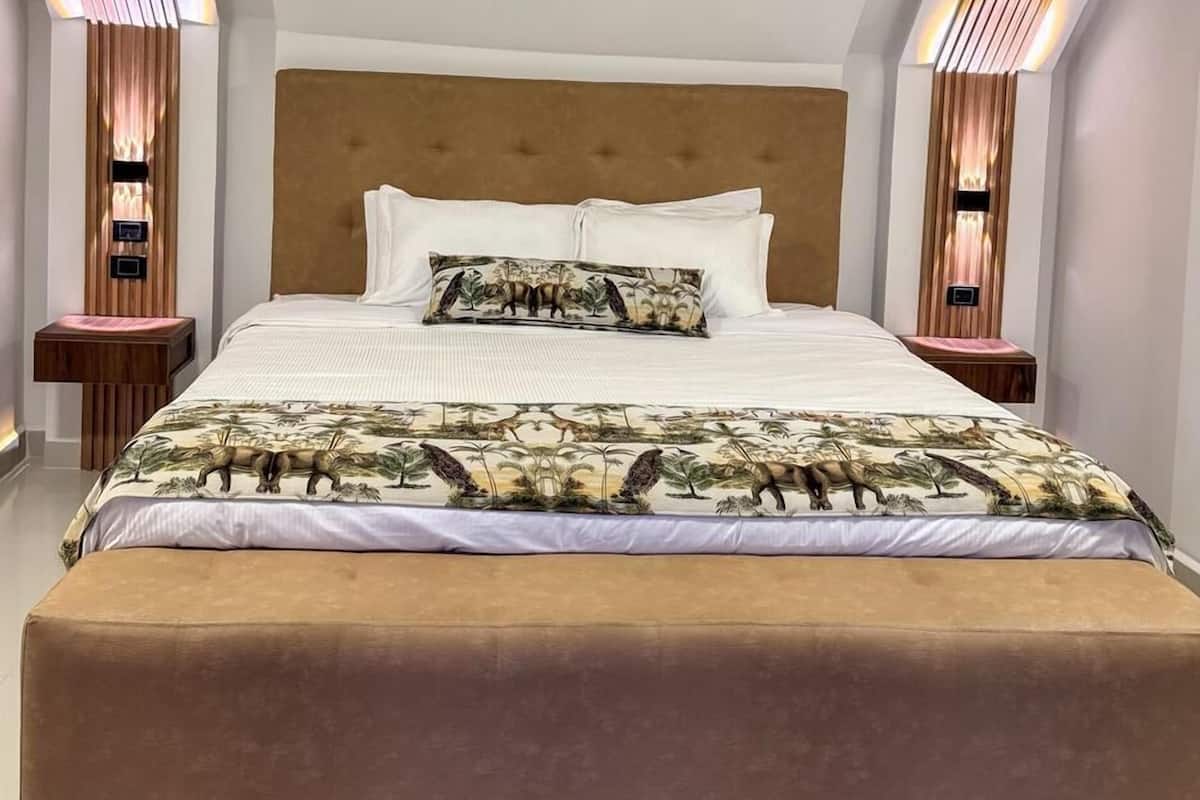 Une chambre à coucher avec un grand lit, une tête de lit et deux tables de chevet dotées d’un éclairage intégré.