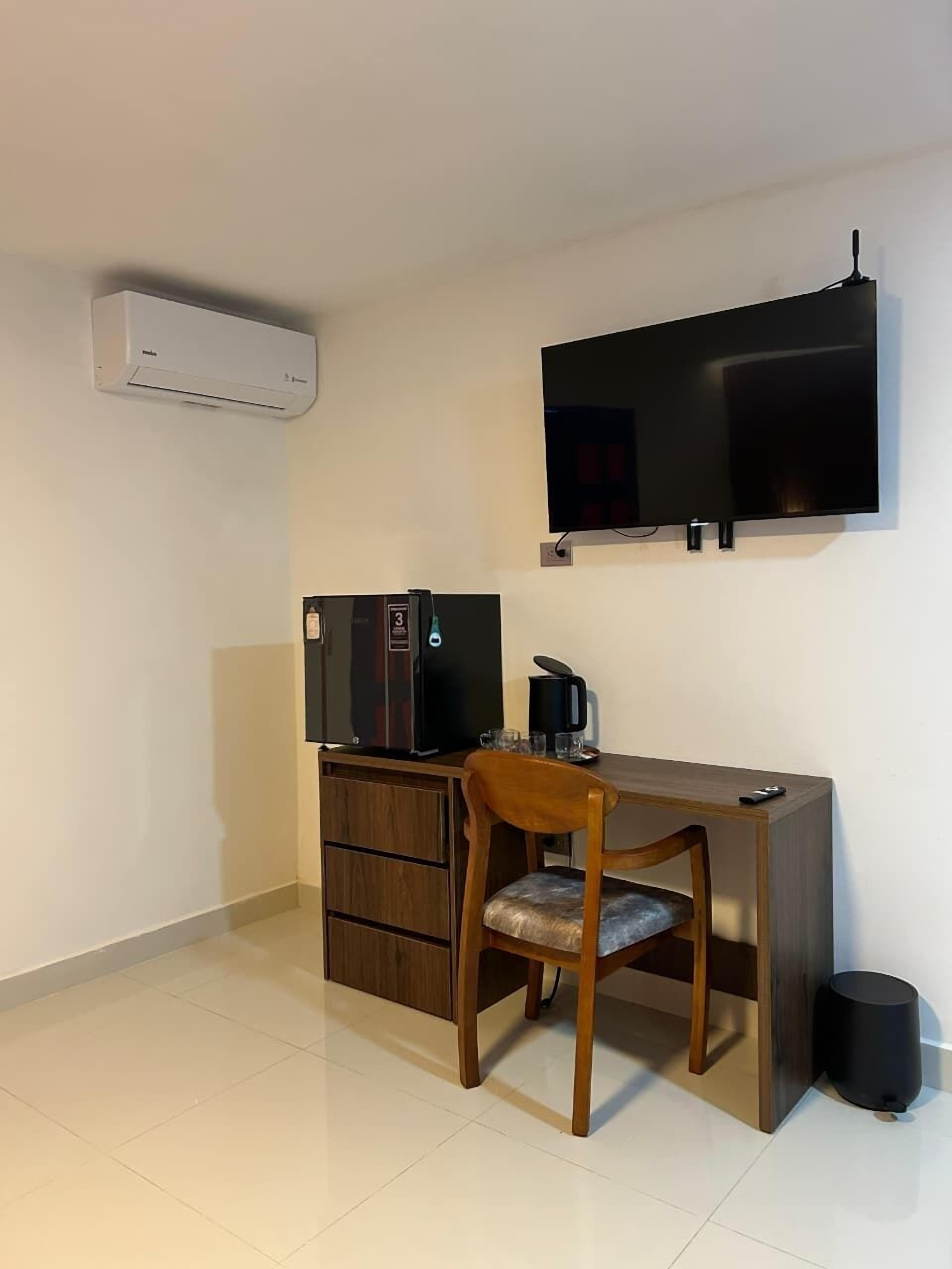 Habitació petita i ordenada amb escriptori, cadira, televisió, aire condicionat i paperera.