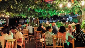 An outdoor dining area with wooden tables and chairs, surrounded by lush greenery and hanging lights. - MAHAWI RESORT (Calarca)