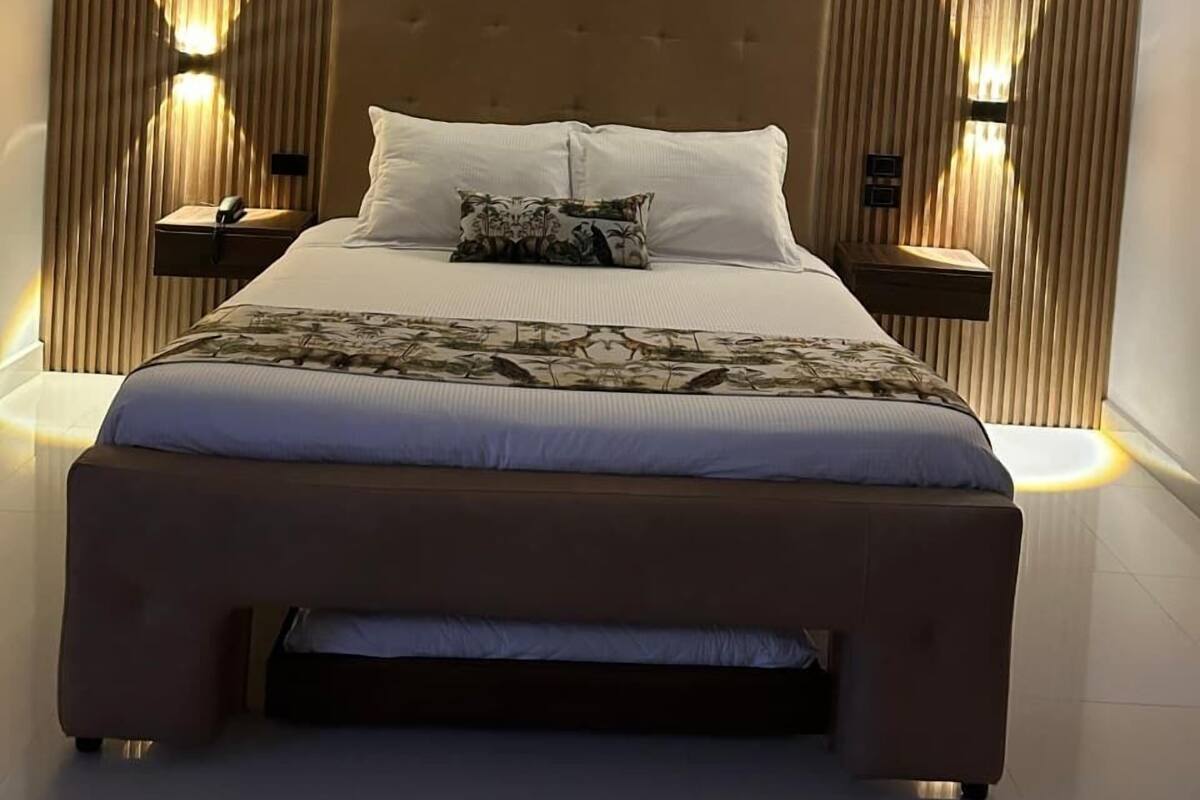 Une chambre moderne avec un grand lit, deux tables de chevet et des stores verticaux.