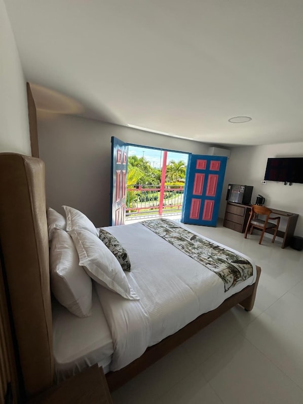 A bedroom with a bed, a desk, a chair, a TV, and a balcony with a view of greenery. - MAHAWI RESORT (Calarca)