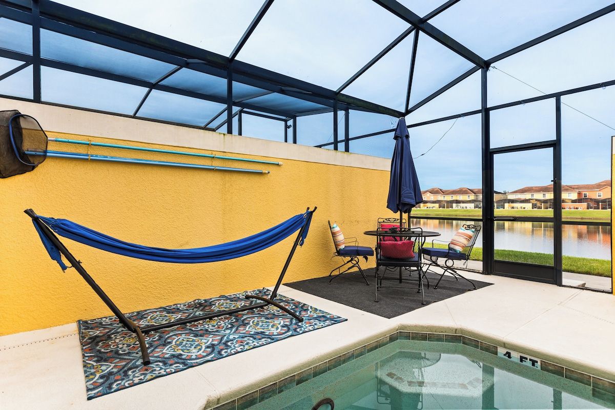 An indoor swimming pool area with a hammock, chairs, and a view of a lake.