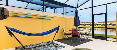 An indoor swimming pool area with a hammock, chairs, and a view of a lake.