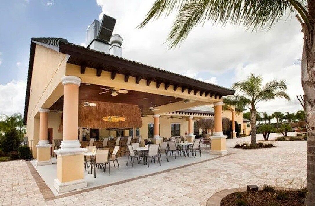 An outdoor patio area with multiple tables and chairs, a covered seating area, and a building with a tiled roof.