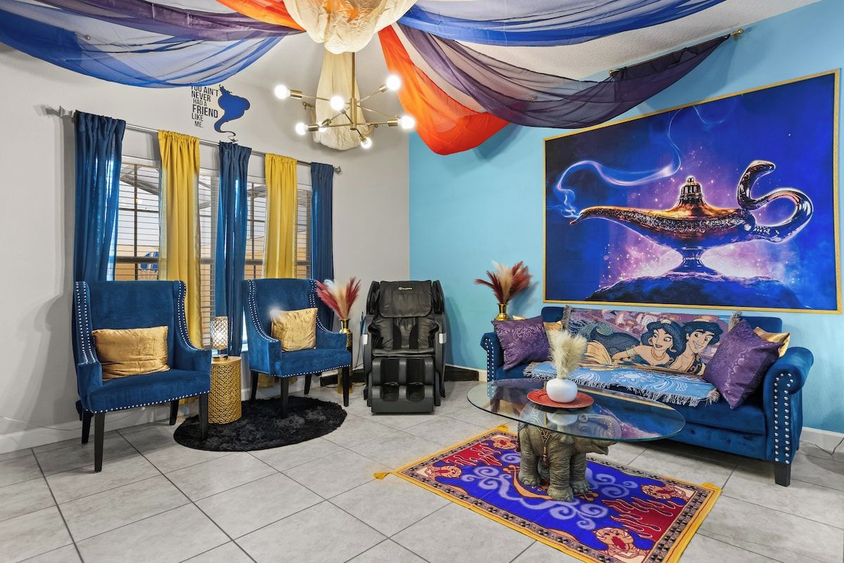 A living room with a blue sofa, a massage chair, a glass coffee table, and a large painting of a genie lamp.