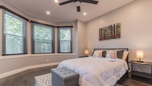 Ein Schlafzimmer mit einem großen Bett, zwei Nachttischen mit Lampen, einem Deckenventilator und einem Gemälde an der Wand.