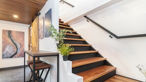 A modern staircase with wooden steps and black handrails, a wooden table with a plant, and abstract art on the walls. - Manila Luxury Suites 401 (Medellín)