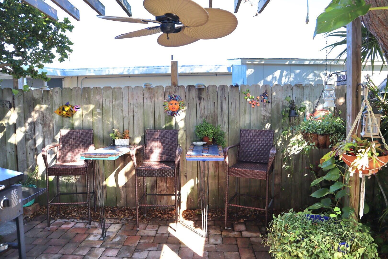 A patio with three wicker chairs, a table, and a ceiling fan.