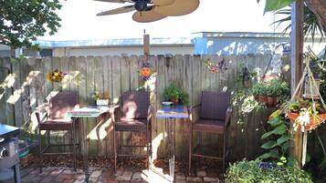 A patio with three wicker chairs, a table, and a ceiling fan.