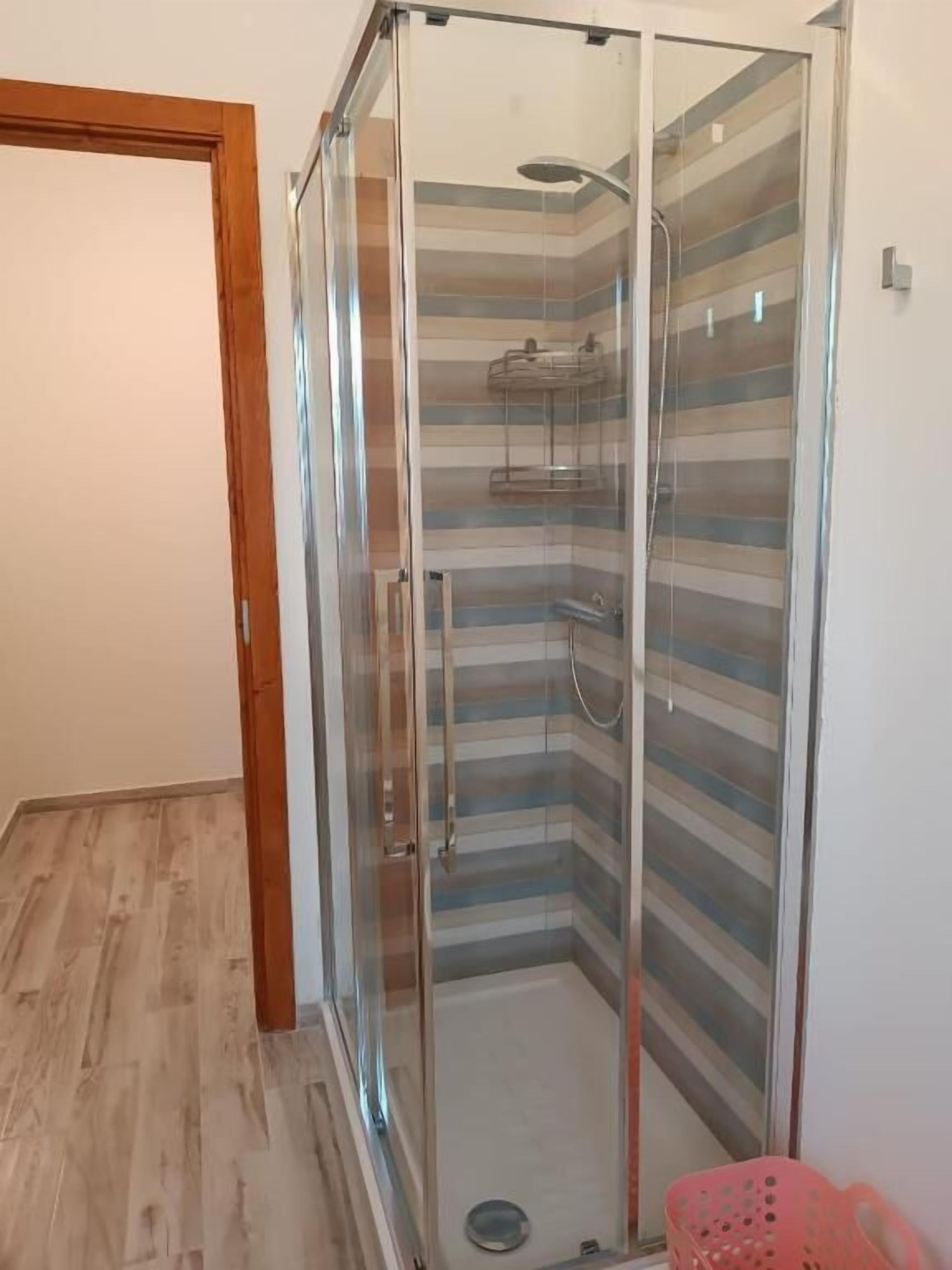 Un box de ducha con paredes de azulejos a rayas, un cabezal de ducha y un rociador de mano.