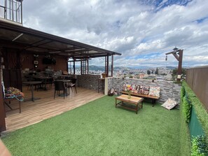 A rooftop patio with a wooden deck, seating area, and a view of a cityscape.