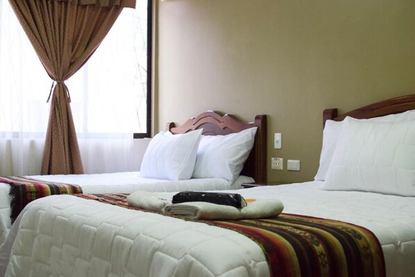 A hotel room with two beds, a window with curtains, and a wall switch.