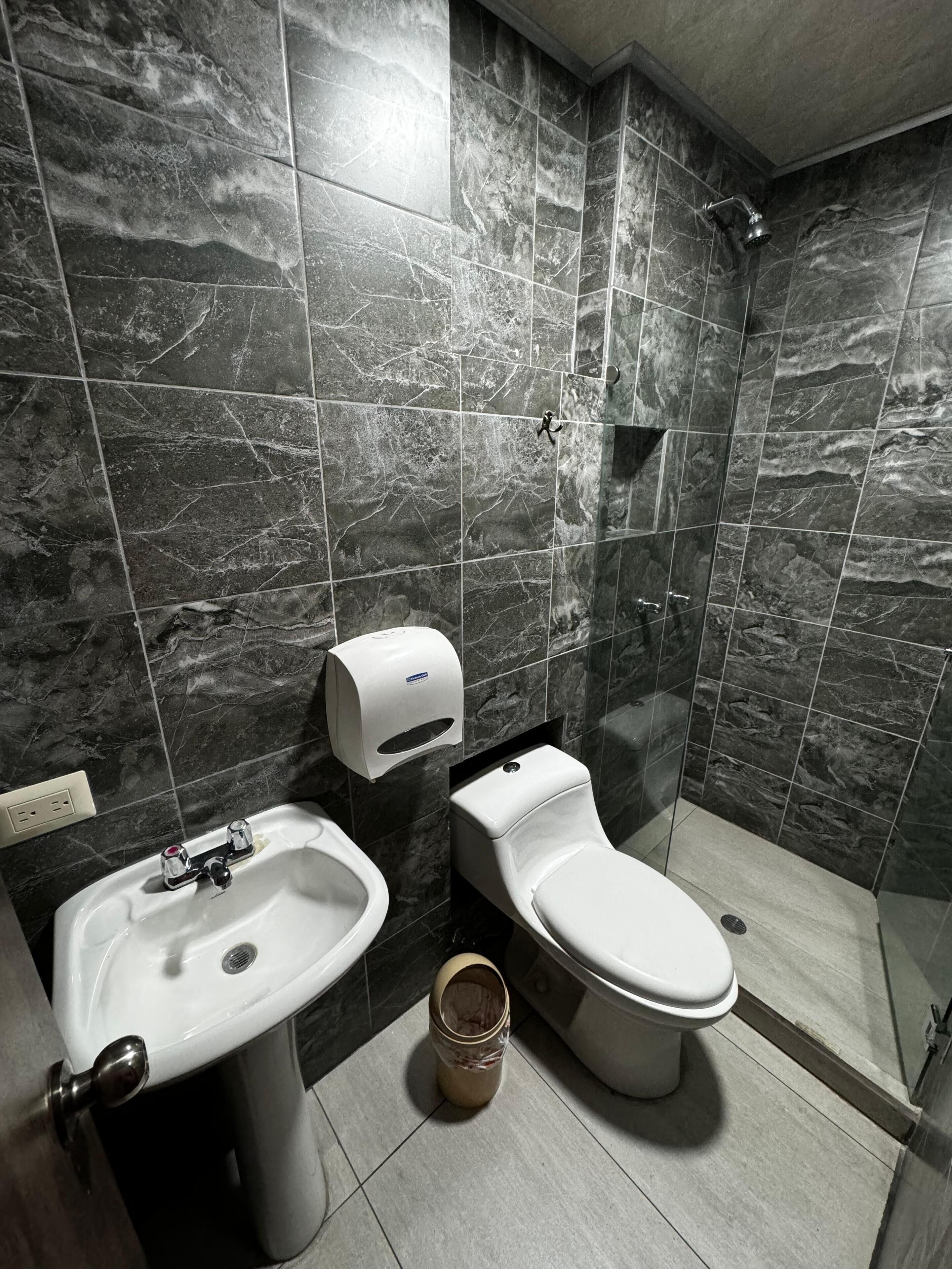 A modern bathroom with a marble tile wall, a sink, a toilet, and a shower.