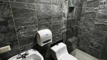Un baño moderno con pared de azulejos de mármol, un lavamanos, un inodoro y una ducha.