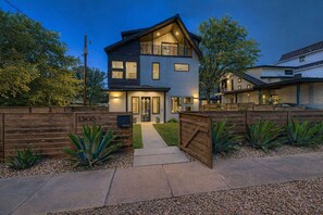A modern two-story house with a well-lit entrance, a wooden fence, and a mailbox. - East Austin 4BR with Hot Tub and Cold Plunge (Austin)