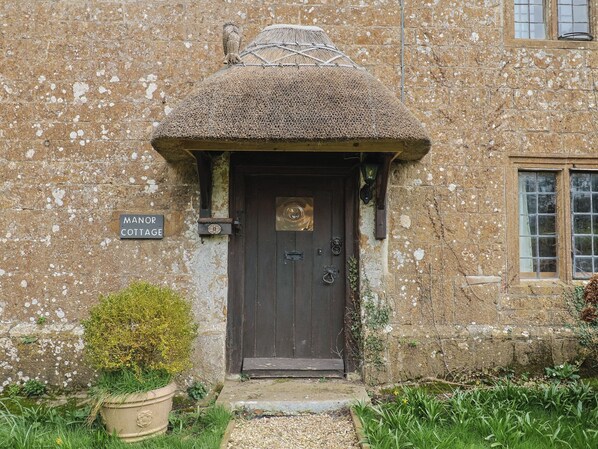Une petite maison en pierre avec un toit de chaume, une porte en bois et une enseigne indiquant « MANCOTTAGE ».