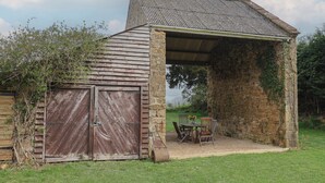Un bâtiment rustique en pierre, doté d’une porte en bois et d’un espace extérieur abrité avec des sièges.