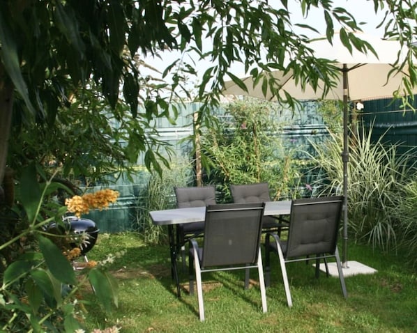 Um pátio externo com mesa e cadeiras, rodeado por vegetação e um cercado.