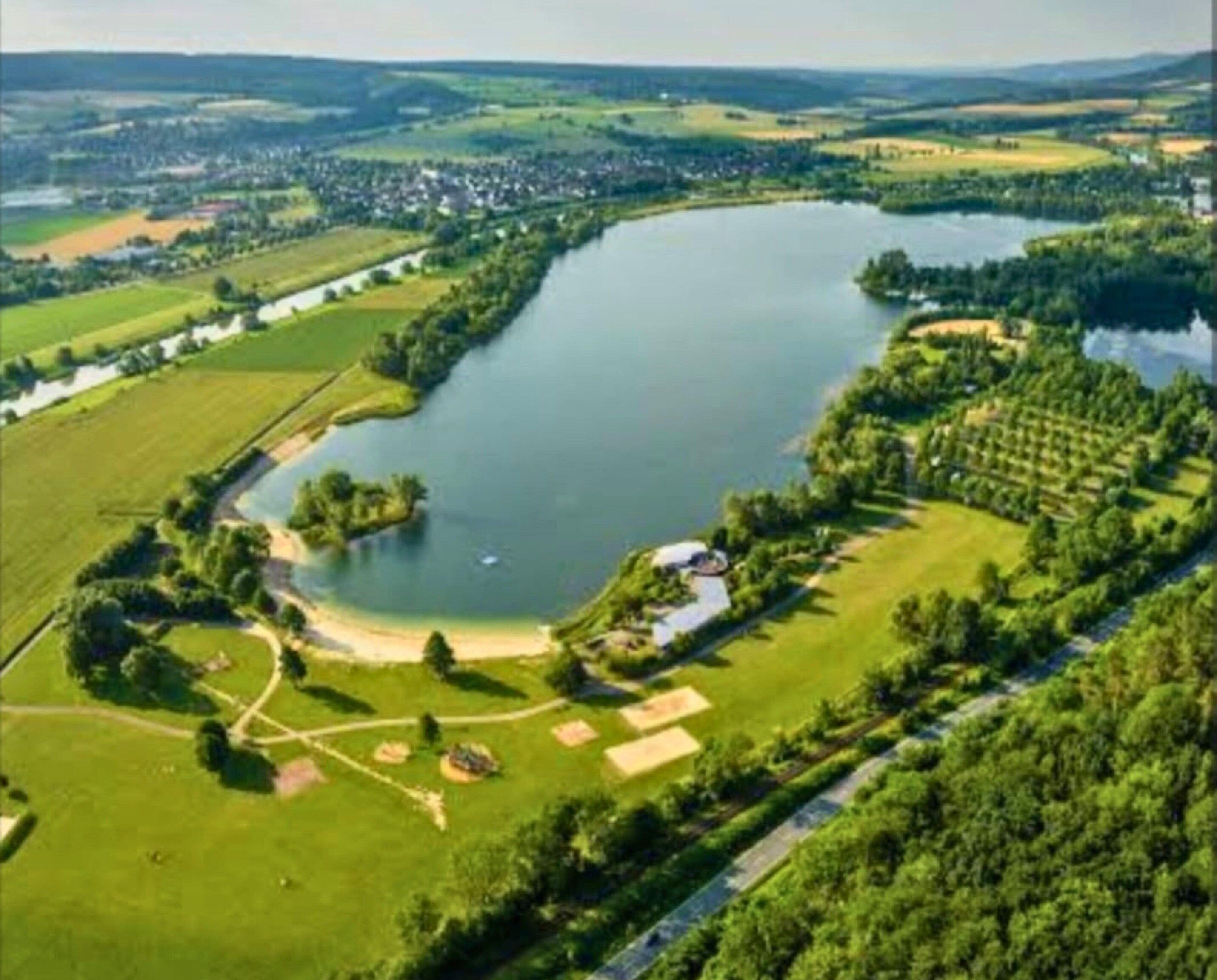 An aerial view of a lake surrounded by green fields and a small settlement.